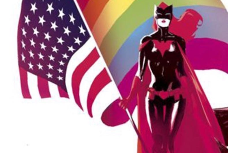 Batwoman stands in front of the American and rainbow flags.